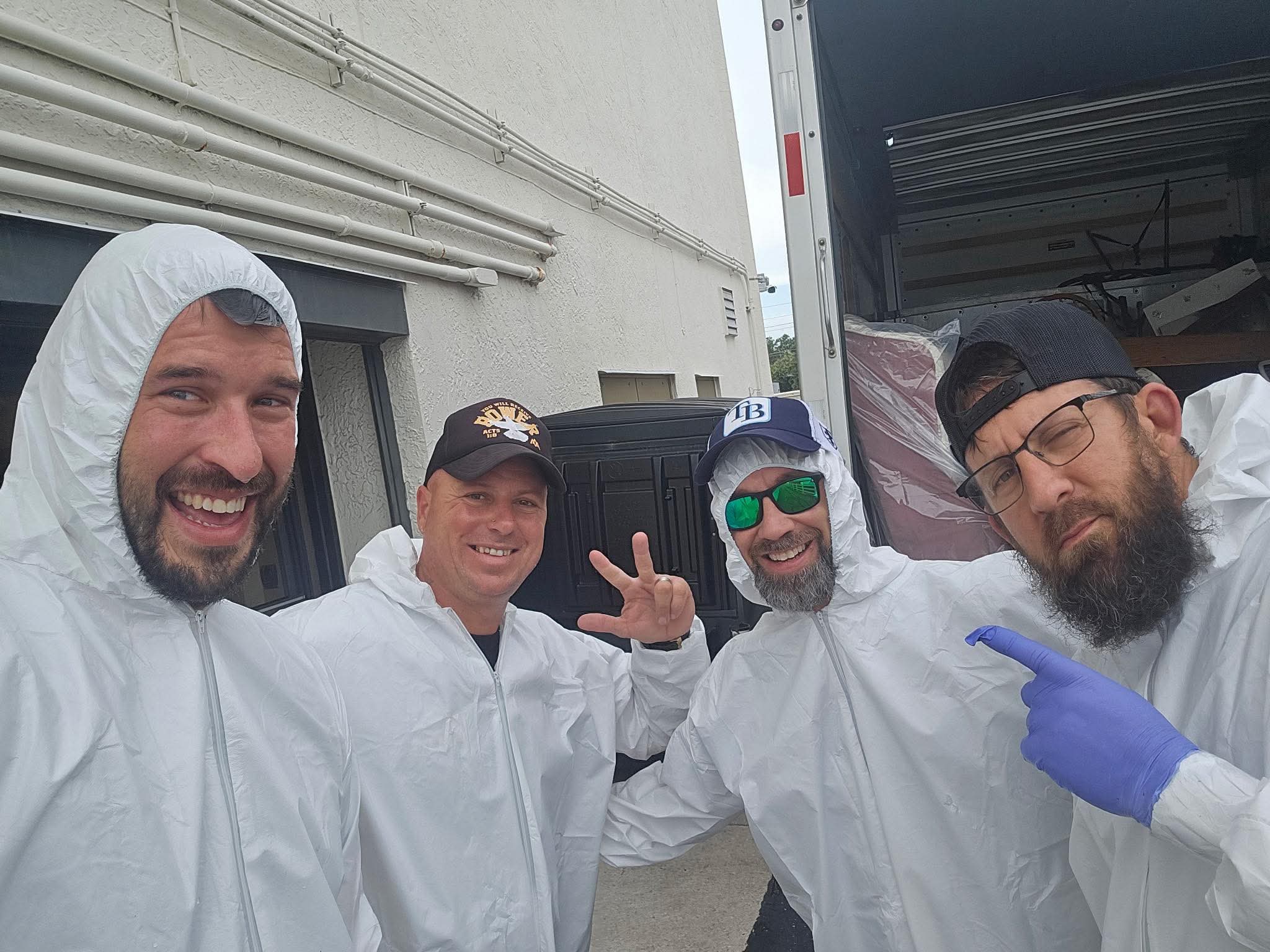 Greg and three men in protective coveralls beside a truck during a community service project.